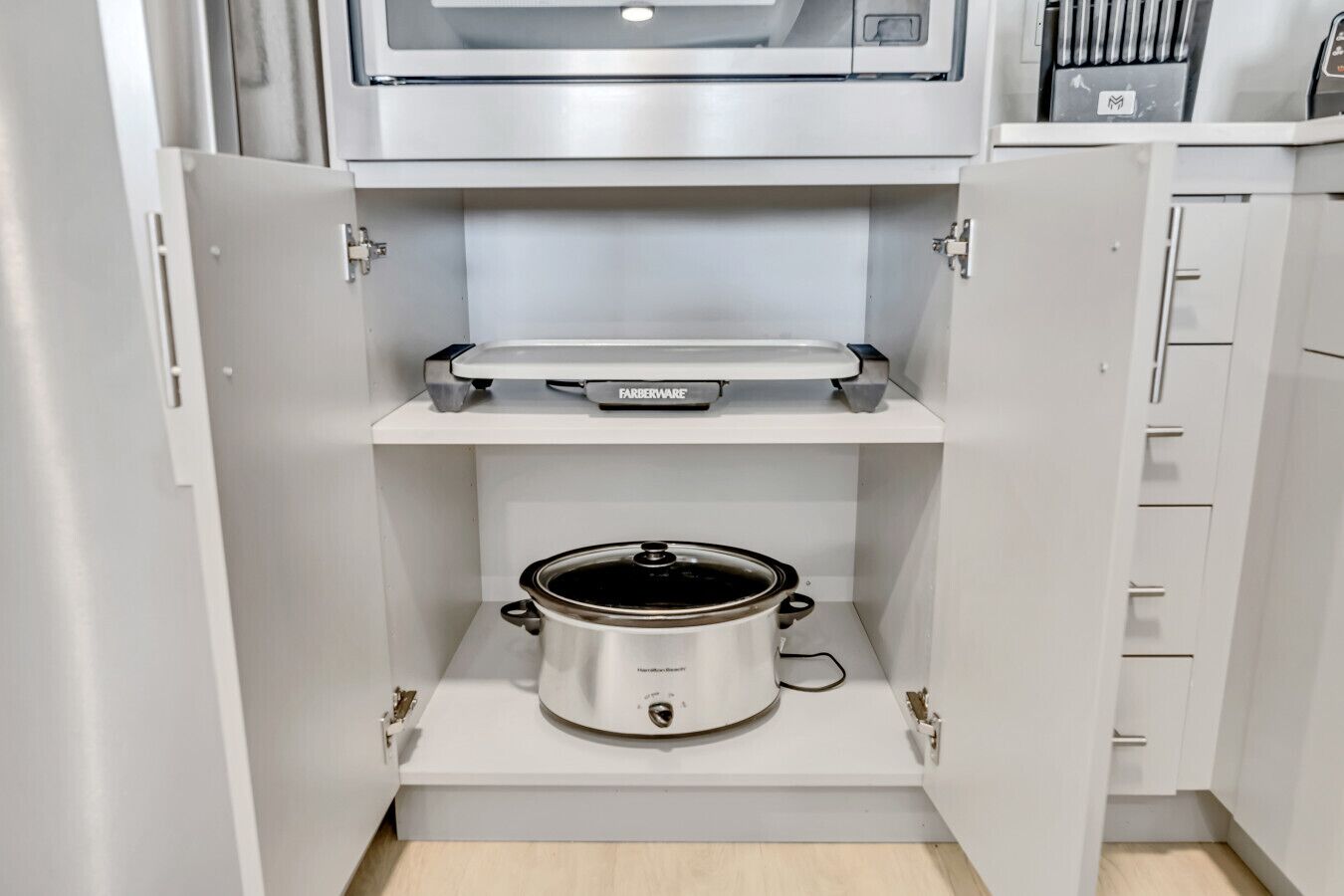 Een keuken met een inbouwoven, een magnetron en een slowcooker.
