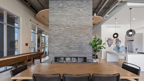 Ein moderner Essbereich mit einem langen Holztisch, schwarzen Stühlen, einer Wand mit Steinakzenten und einer Küche im Hintergrund.