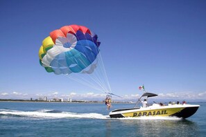 A parasail with a colorful canopy, a boat with 'PARASAIL' written on it, and a clear blue sky in the background. - Cozy Studio With sea View in Lignano Sabbiadoro (Lignano Sabbiadoro)