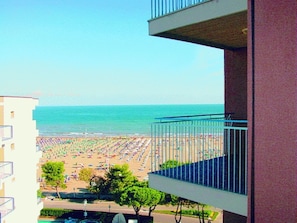 A view of a beach with umbrellas and people from a balcony overlooking the sea.