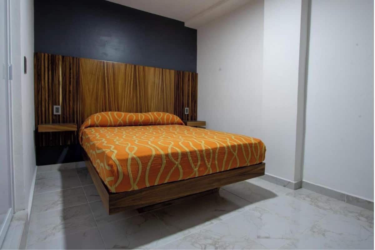 A bedroom with a bed, wooden headboard, and a white wall.