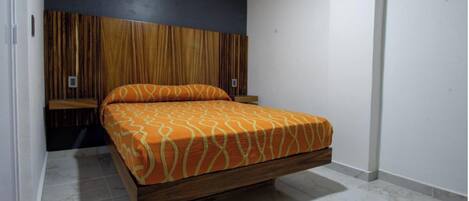 A bedroom with a bed, wooden headboard, and a white wall.