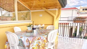 A covered patio with a table set for two, featuring a floral tablecloth and white chairs.