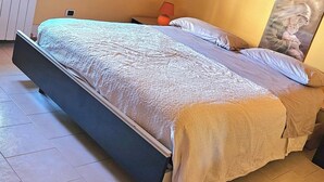 A bedroom with a sloped ceiling, a bed with a patterned bedspread, a nightstand with a lamp, and a painting on the wall.