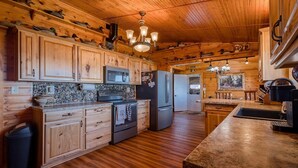 A wooden cabin-style kitchen with wooden cabinets, a granite countertop, a stove, a refrigerator, and a microwave.