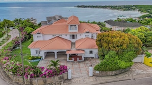 A large, white building with a red-tiled roof, surrounded by lush greenery and a view of the sea. - Large Seaview 3 Bedroom Villa with Private Pool, Terrace & Parking (Discovery Bay)