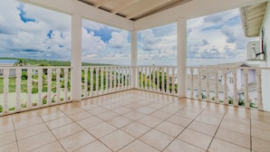 A covered balcony with tiled flooring and white railings, overlooking a green landscape and a body of water. - Large Seaview 3 Bedroom Villa with Private Pool, Terrace & Parking (Discovery Bay)