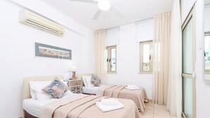 Ein Hotelzimmer mit zwei Betten, einem Deckenventilator, einer Klimaanlage, einem Bild an der Wand und Blick durch das Fenster.