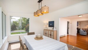 Una habitación amplia con un gran ventanal, una mesa de comedor con un centro decorativo tejido y un mueble de madera con un televisor de pantalla plana.