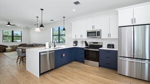 A modern kitchen with white and blue cabinets, stainless steel appliances, and a central island. - Ocean Oasis (Fort Myers Beach)