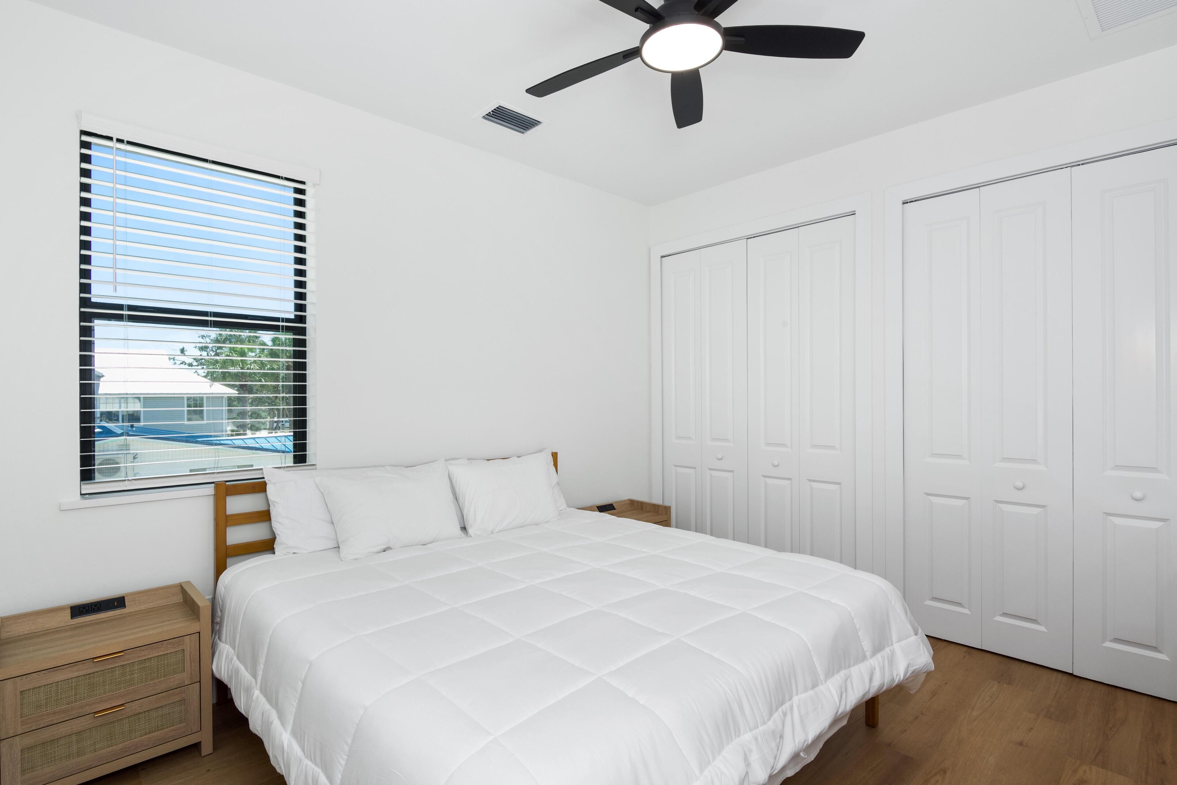 A bedroom with a bed, a ceiling fan, a window with blinds, and a wardrobe.