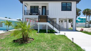 A modern two-story house with a balcony, a staircase, and a small garden area. - Ocean Oasis (Fort Myers Beach)