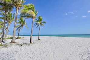A beach with white sand and palm trees under a clear blue sky. - Ocean Oasis (Fort Myers Beach)