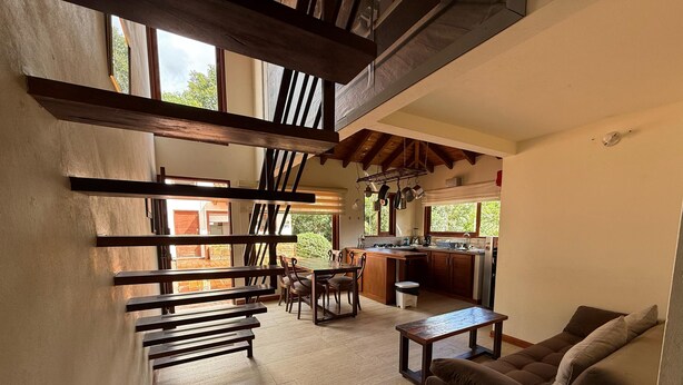 Amplia sala de estar con una mesa de comedor, bancos de madera, un sofá y una cocina con un lavamanos y armarios.