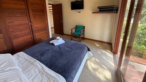 Un dormitorio con cama, un armario de madera, televisión en la pared y una silla.