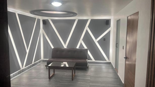 Un vestíbulo moderno con un sofá de cuero oscuro, una mesita y un diseño geométrico en la pared.