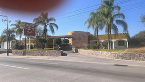 Entrada de un hotel con un cartel que dice "AUTO HOTEL Yucatan" y un muro de piedra con palmeras.