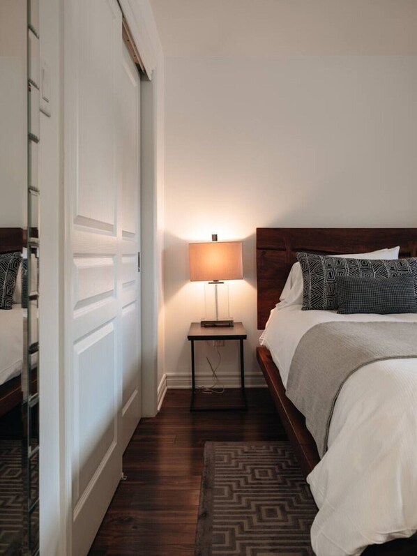 A hotel room with a bed, bedside table with a lamp, a wooden headboard, and a patterned rug.
