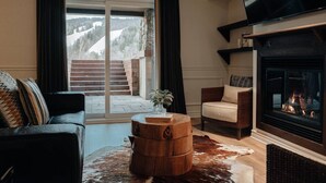 Una sala de estar con chimenea, un sofá, una silla y un ventanal con cortinas.