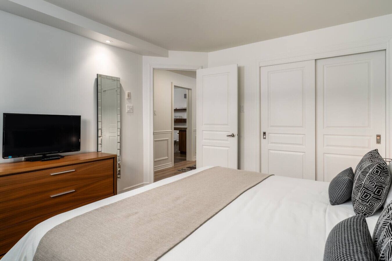 A bedroom with a bed, a TV on a wooden dresser, and white doors.