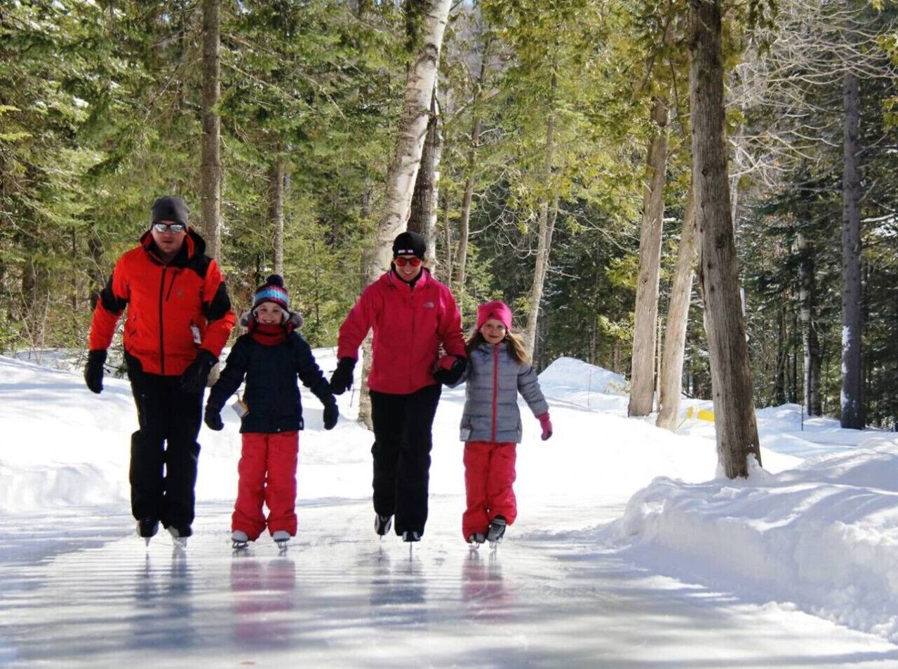 Una familia de cuatro personas patinando sobre un lago helado rodeado de árboles.