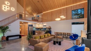 A spacious living area with a high ceiling, wooden beams, a built-in kitchen, and a staircase to an upper level.