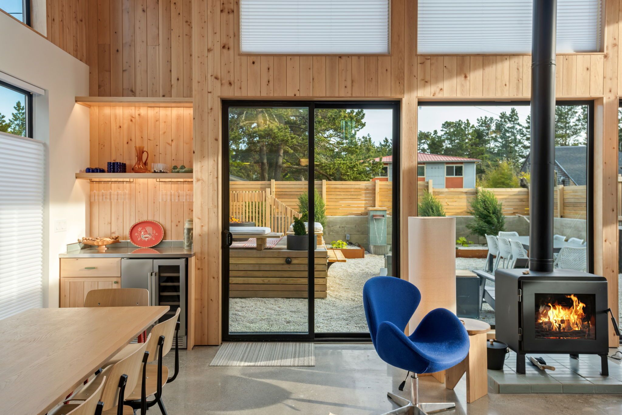 Een moderne keuken met houten wanden, een grote schuifglazen deur naar een terras en een houtkachel.