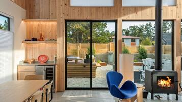 Een moderne keuken met houten wanden, een grote schuifglazen deur naar een terras en een houtkachel.