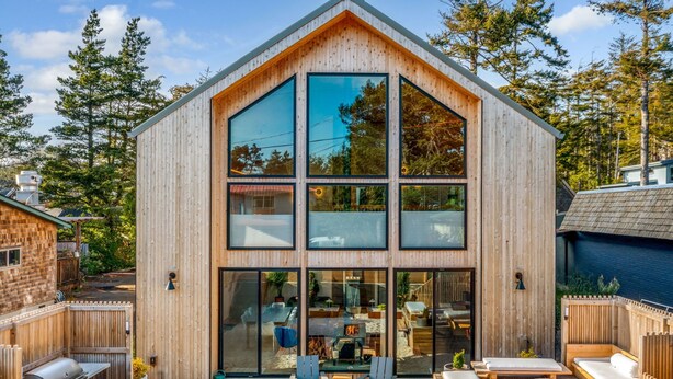 A modern wooden cabin with large windows, a patio with outdoor seating, and a fire pit.