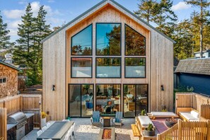 Ein modernes Holzhaus mit großen Fenstern, einer Terrasse mit Gartenmöbeln und einem sichtbaren Küchenbereich.