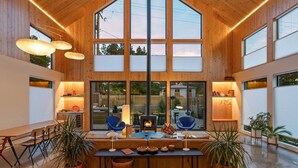 A spacious room with a large wooden ceiling, multiple windows, and a central table with chairs.