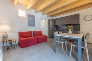 Un salon moderne avec un canapé, une table à manger et des chaises. On y trouve également un coin cuisine avec des placards et une horloge au mur.