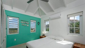 Une chambre à coucher avec un lit, une table de chevet, une fenêtre donnant sur un beau paysage et un ventilateur de plafond.
