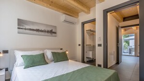 A bedroom with a bed, a green blanket, a cityscape painting, and a hallway leading to an outdoor area. - GuestHost - Le Agavi - Lovely Flat X6 with Terrace (Ferrara)