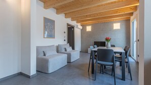 A modern interior with a wooden ceiling, grey sofas, a dining table with chairs, and a vase with flowers. - GuestHost - Le Agavi - Lovely Flat X6 with Terrace (Ferrara)