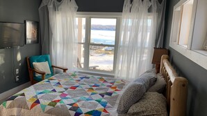 Un dormitorio con una cama grande, una silla, un televisor y vistas a la playa.
