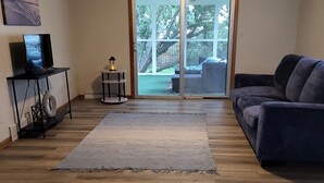 A living room with a wooden floor, a dark blue couch, a television on a stand, and a ceiling fan.
