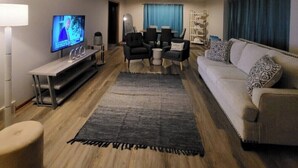 A modern living room with a flat-screen TV, a sofa, a coffee table, and a dining area with chairs and a table.