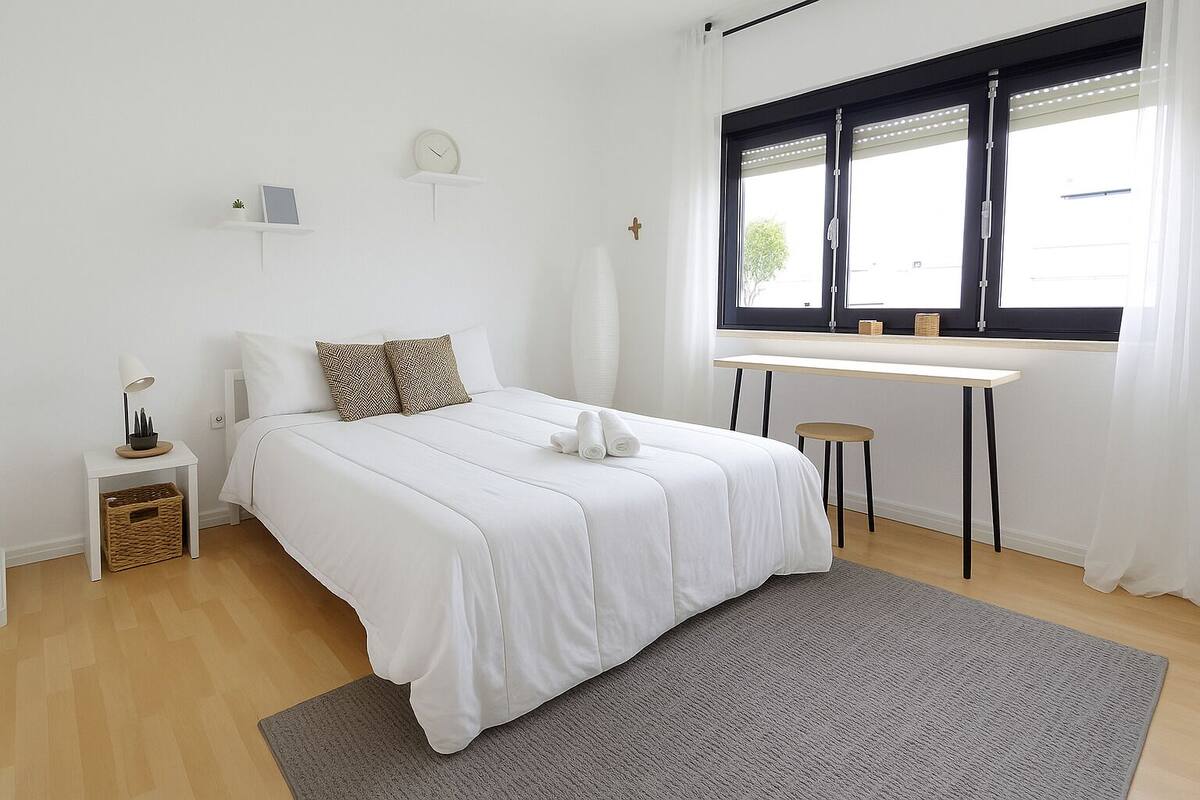 A minimalist bedroom with a bed, bedside table, and a desk by a window.