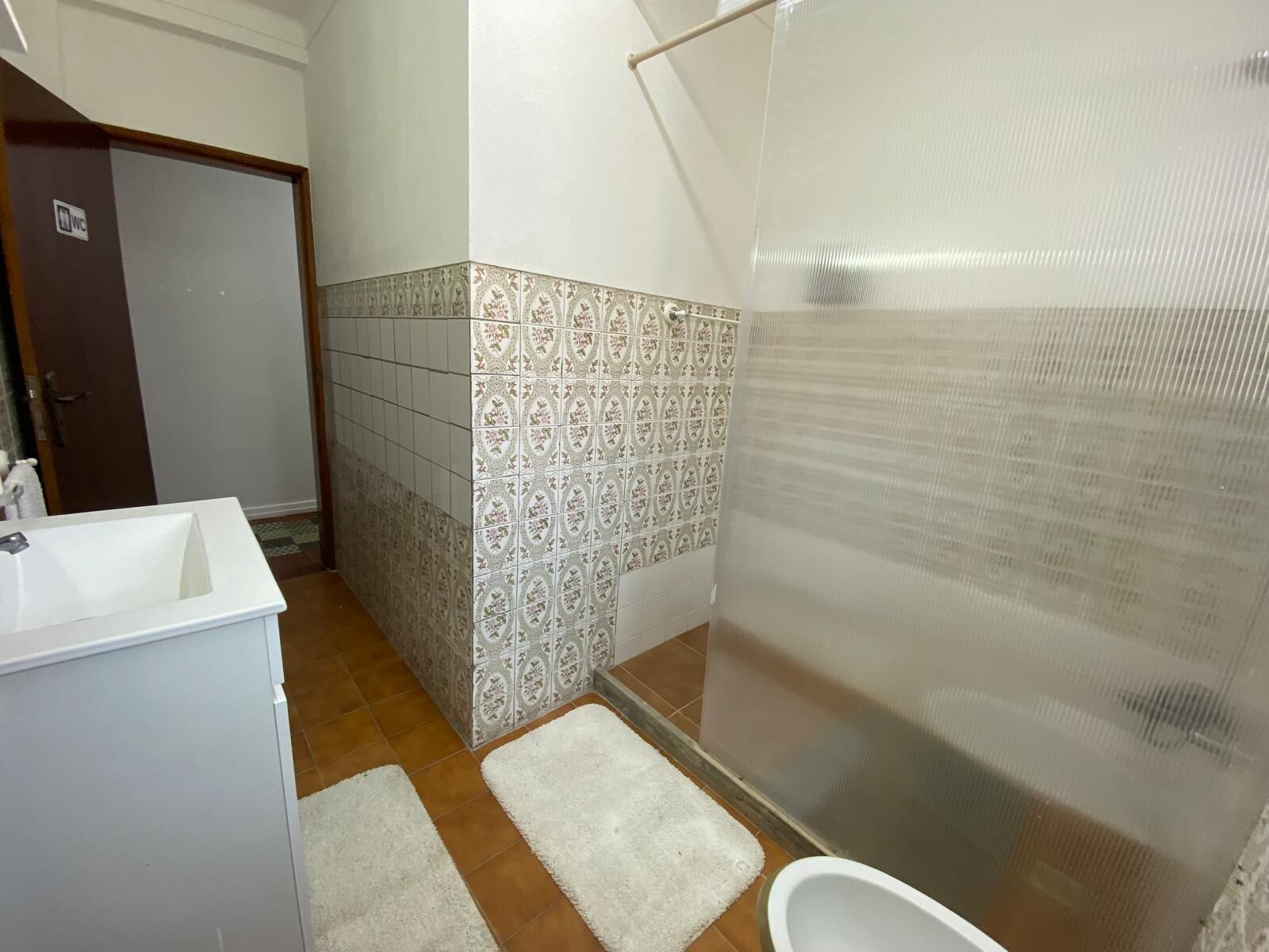 A bathroom with a white sink, a toilet, a shower with a frosted glass door, and patterned tiles on the walls.