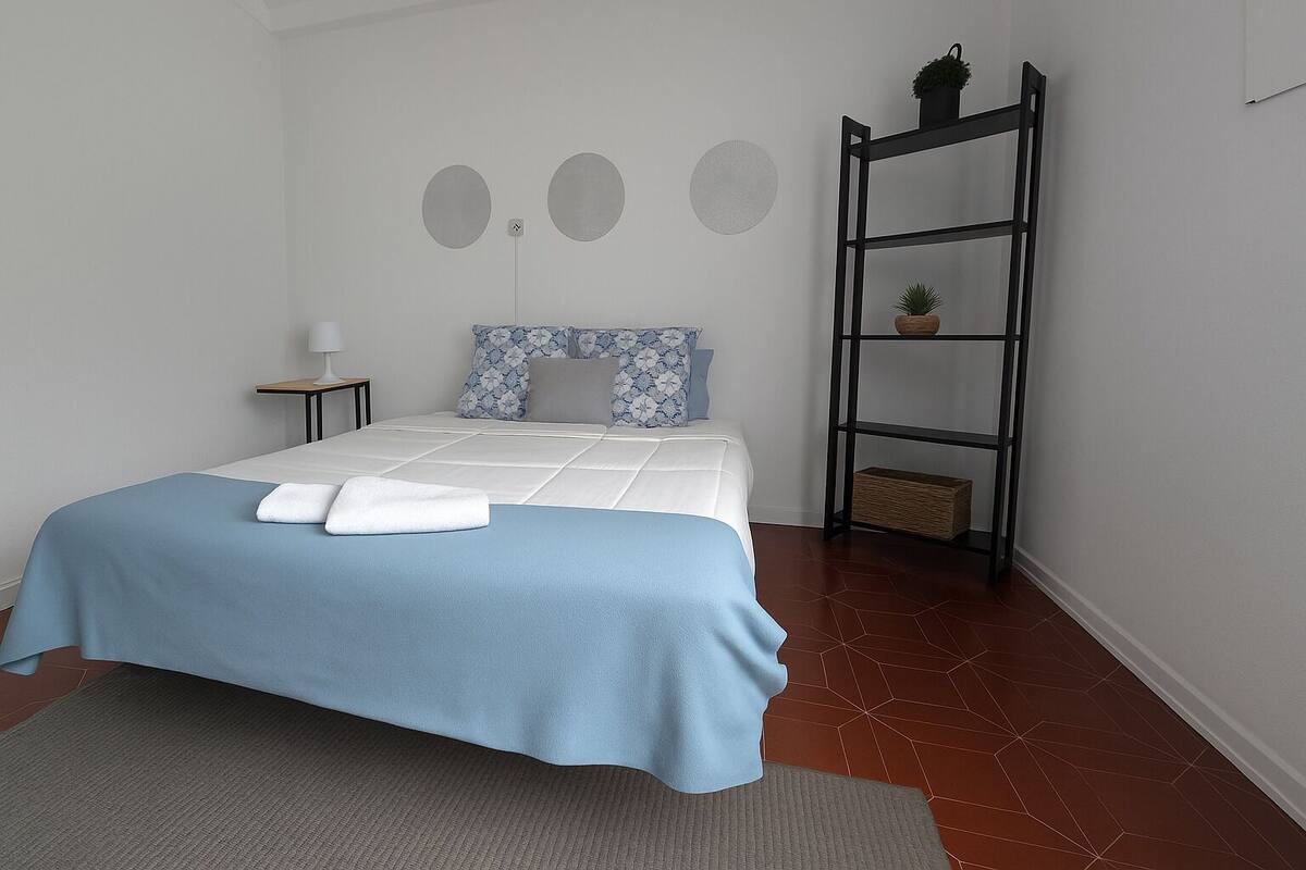 A neatly arranged bedroom with a bed, a bedside table, a wall-mounted shelf with plants, and a geometric-patterned floor.