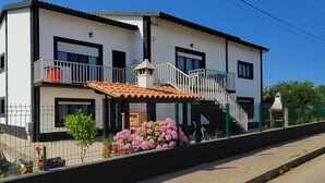 A two-story building with a balcony, a staircase, and a small garden with pink flowers. - Freedom Surf House (Peniche)