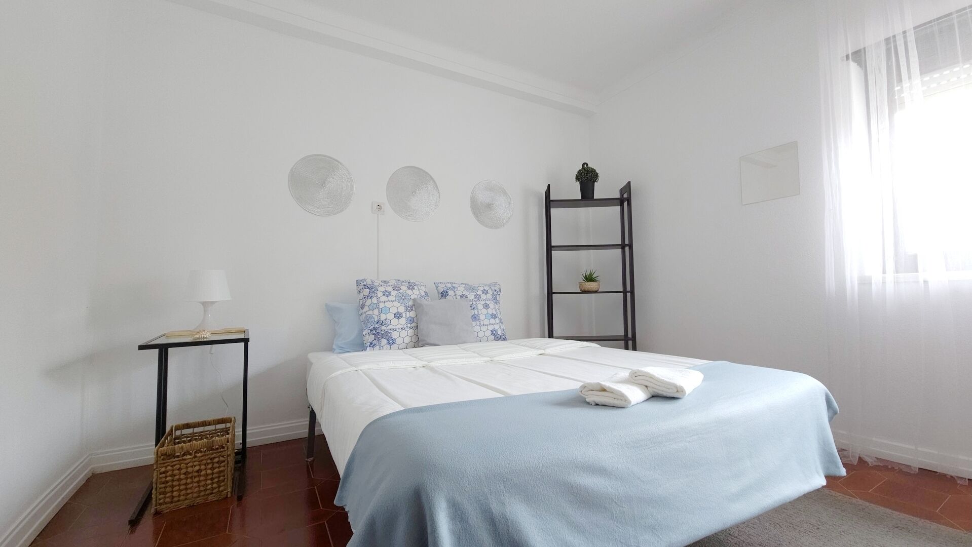 A bedroom with a bed, a nightstand, a lamp, and a small shelf with a plant.
