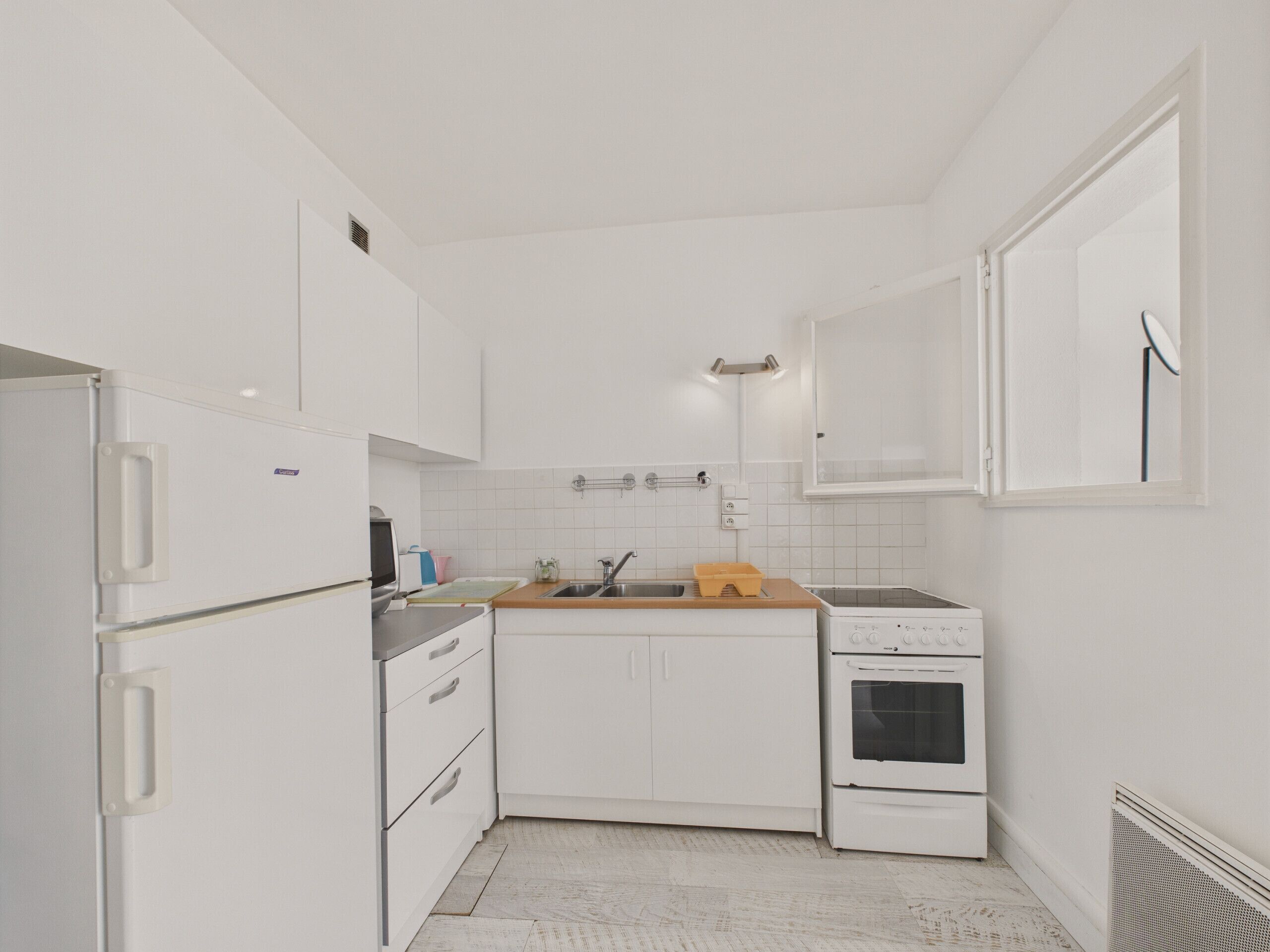 Una cucina compatta con mobili bianchi, forno integrato, lavello e un piccolo ripiano.