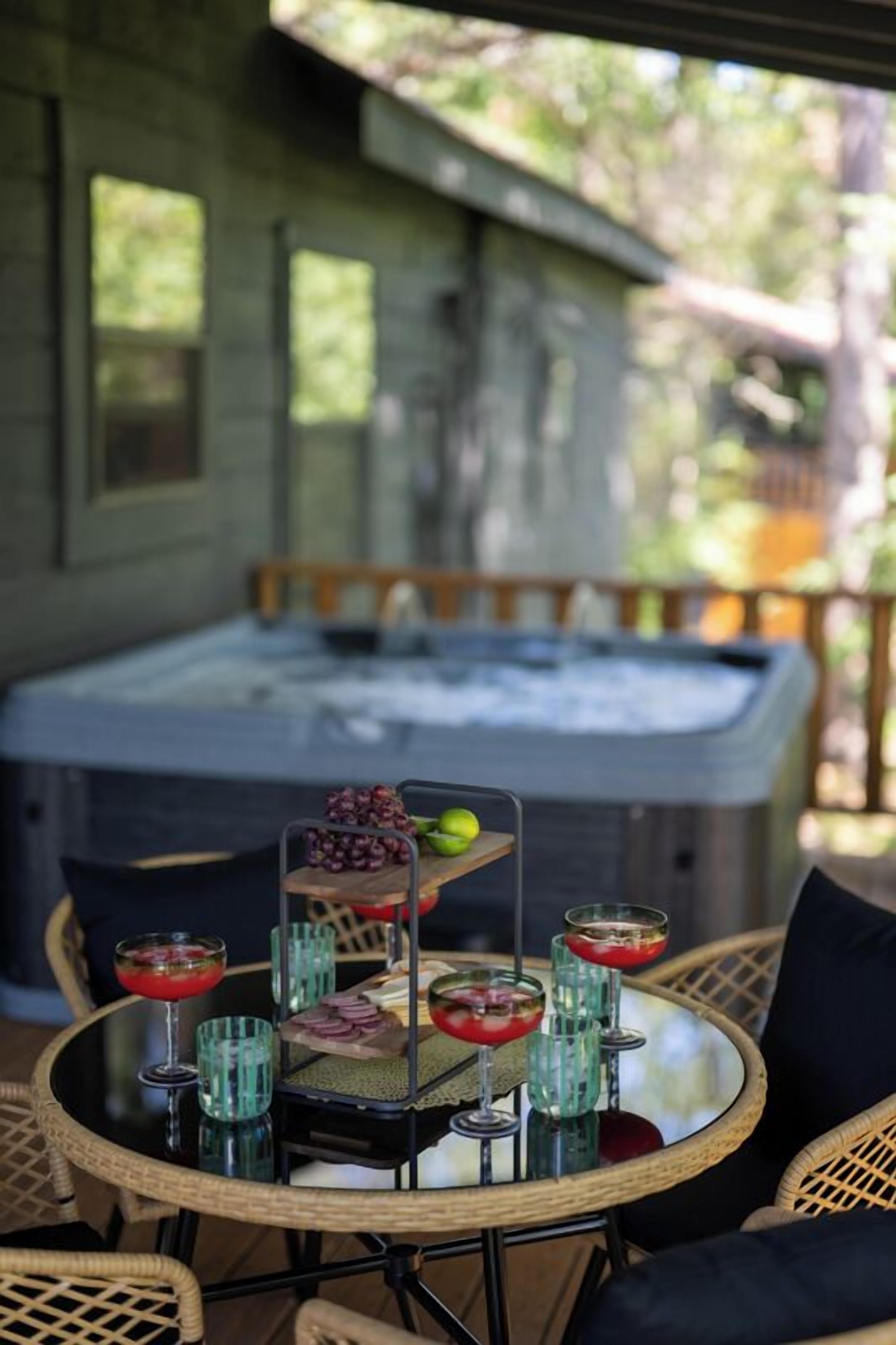 A round table with a glass top, surrounded by wicker chairs, set outdoors with a hot tub in the background.