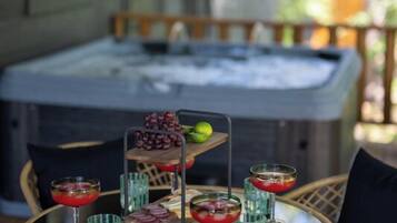 A round table with a glass top, surrounded by wicker chairs, set outdoors with a hot tub in the background.