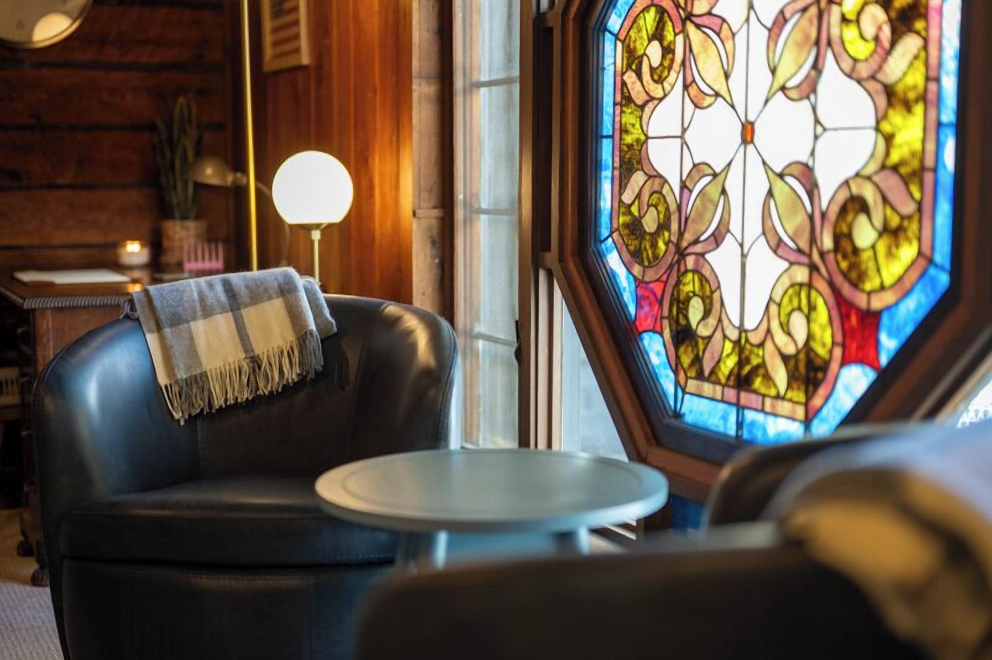 Une pièce chaleureuse avec un canapé en cuir, une petite table ronde et un vitrail.