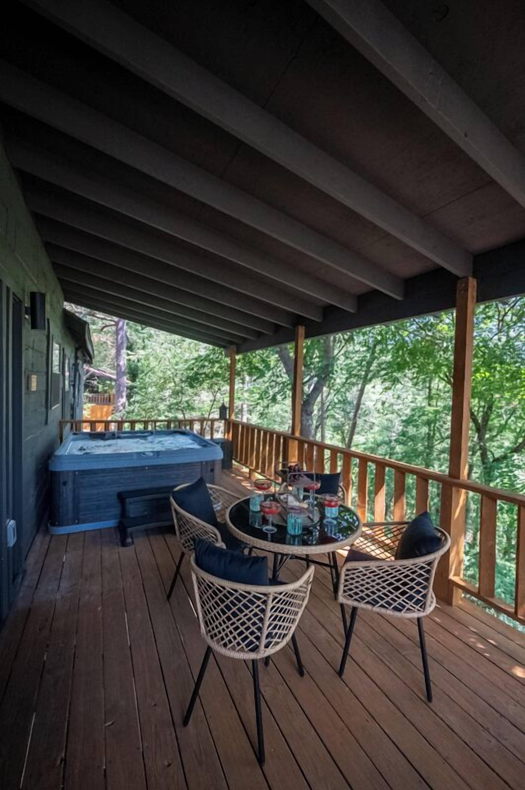 Una terraza de madera con un jacuzzi, sillas de mimbre y una mesa con bebidas.