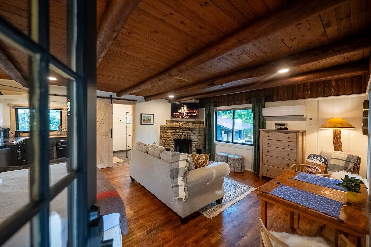 A cozy living room with a fireplace, wooden ceiling, and a dining area with a table and chairs.