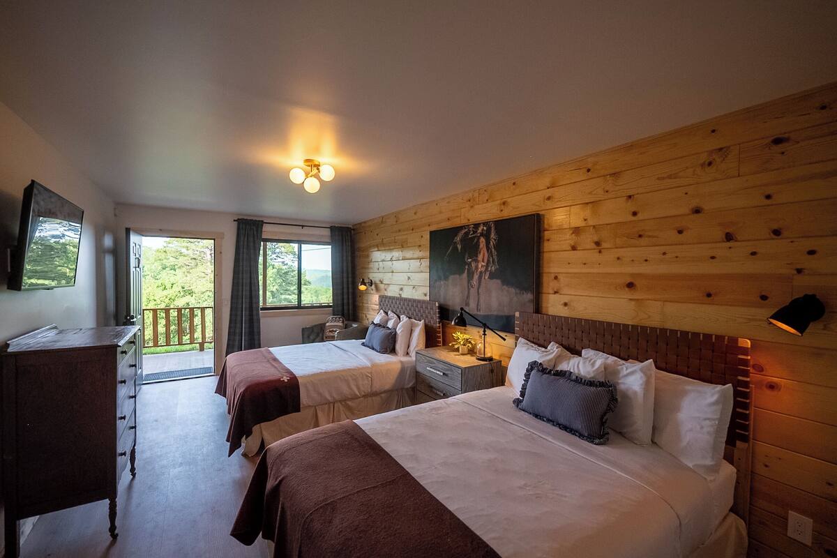 A hotel room with two beds, wooden paneling, a painting on the wall, and a balcony view.